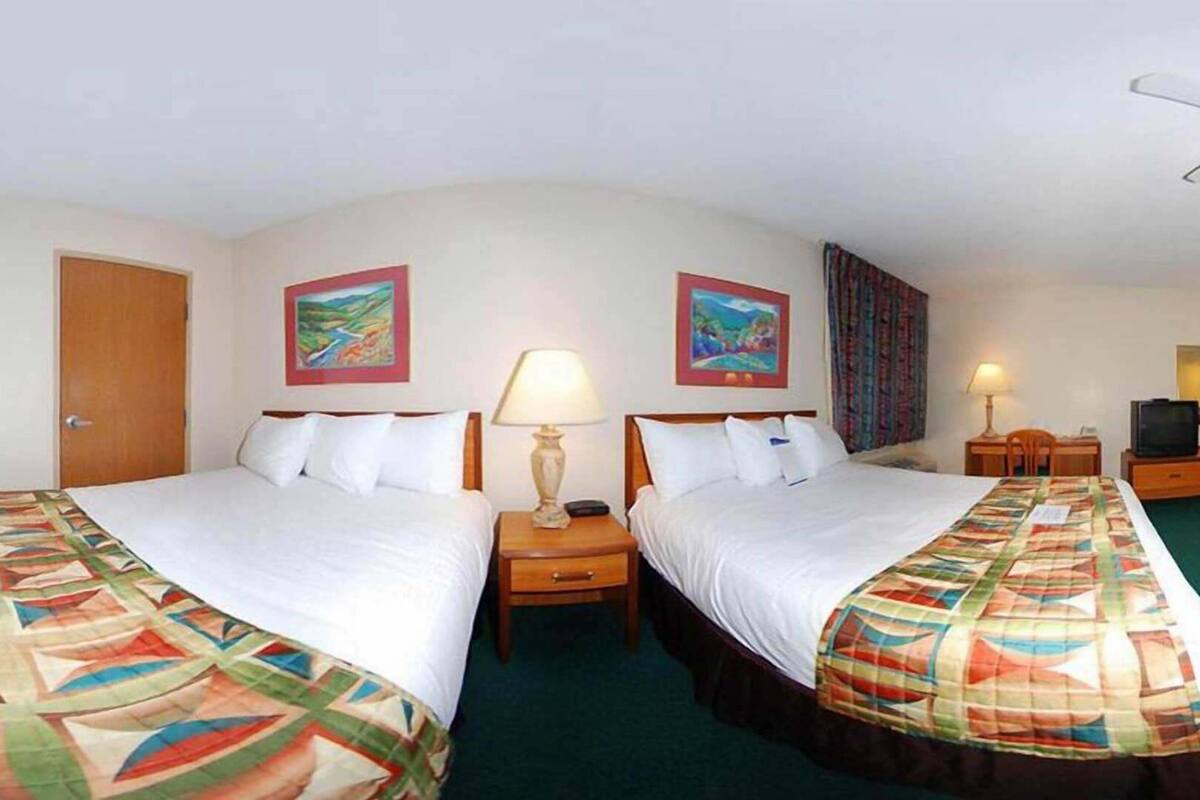 A hotel room with two beds, a desk, a television, and two paintings on the wall.
