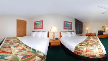 Ein Hotelzimmer mit zwei Betten, jeweils mit farbenfroher Bettdecke, einem Nachttisch mit Lampe, einem Fernseher und Bildern an den Wänden.