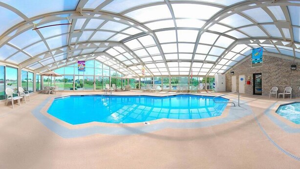 A large indoor swimming pool with a glass ceiling, surrounded by lounge chairs and a stone wall. - Baymont by Wyndham Sullivan (Sullivan)
