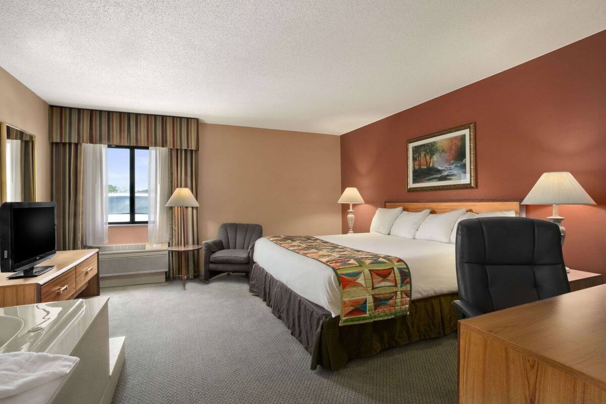 A hotel room with a bed, desk, chair, television, and a window with curtains.