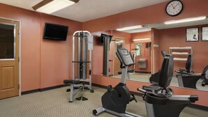A gym with exercise equipment, a clock, and a television on the wall. - Baymont by Wyndham Sullivan (Sullivan)