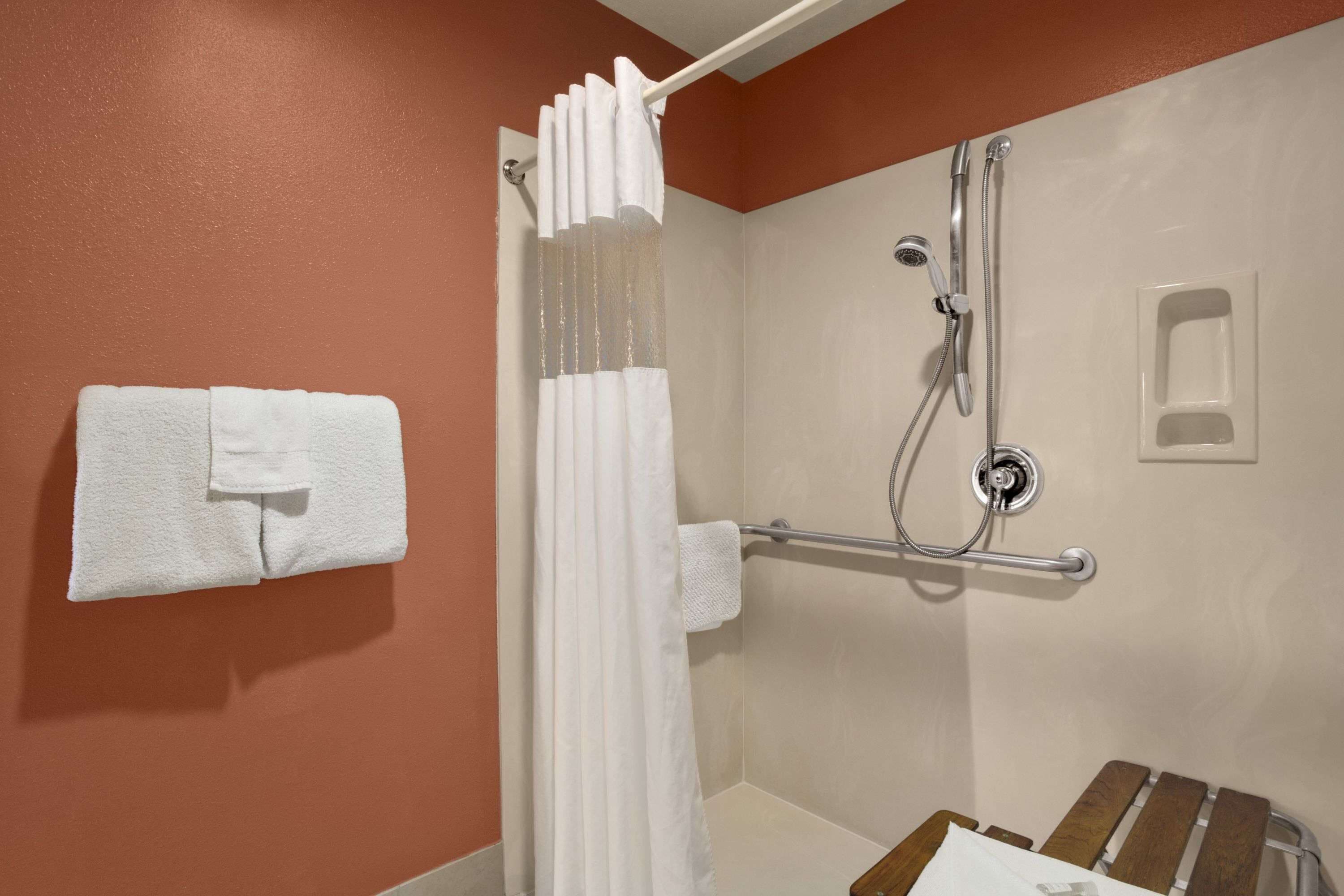 A shower area with a white towel hanging on the wall, a shower curtain, and a grab bar.