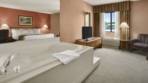 A hotel room with a large bed, a TV on a wooden side table, a desk with a lamp, and a view of the outdoors through a window with curtains. - Baymont by Wyndham Sullivan (Sullivan)