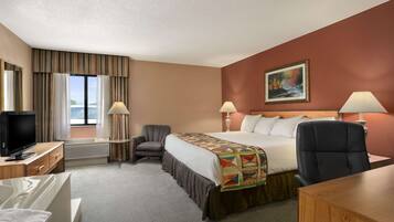 A hotel room with a bed, two chairs, a desk, a TV, and a painting on the wall.