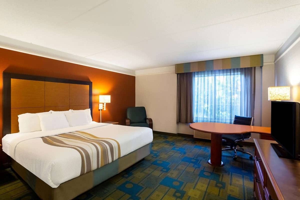 A hotel room with a bed, a desk, a chair, a television, and a window with curtains.