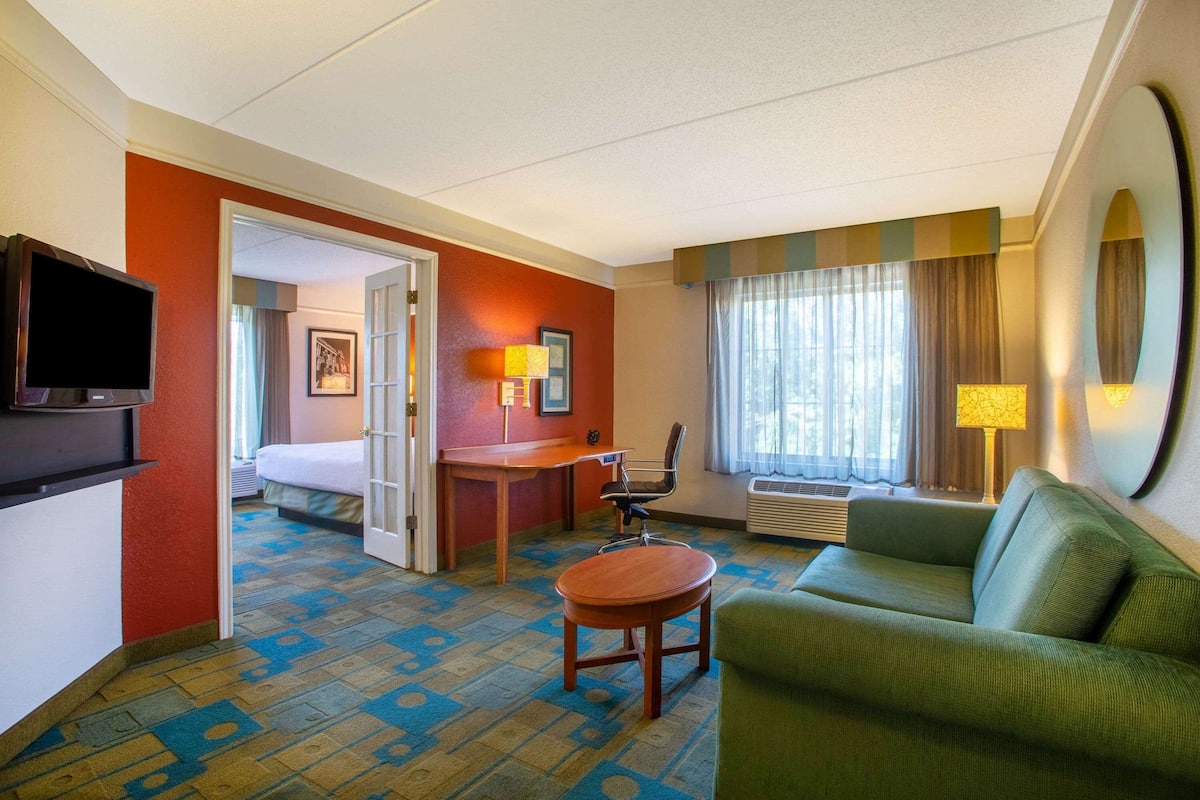 A hotel room with a bed, a desk, a green sofa, a small table, a TV, and a window with curtains.