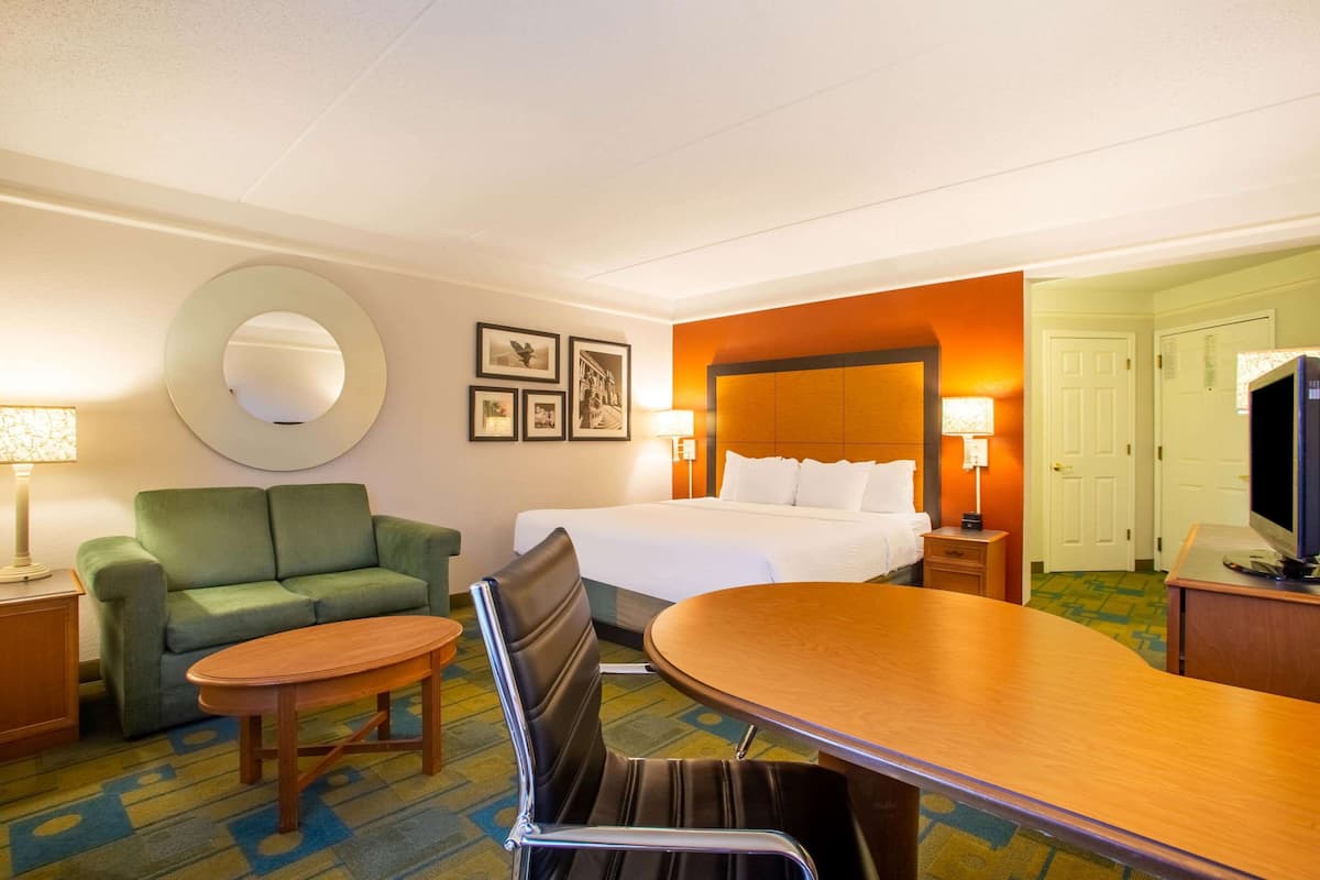 A hotel room with a bed, a green sofa, a wooden table, a round mirror, and two bedside lamps.