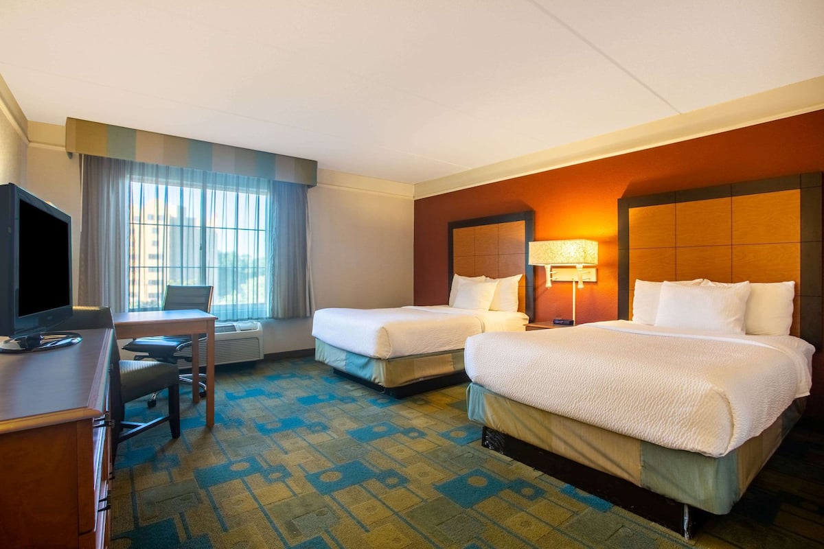 A hotel room with two beds, a desk, a television, and a window with curtains.