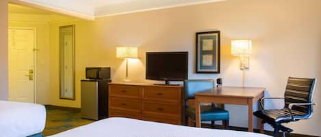 Quarto de hotel com duas camas, uma escrivaninha com cadeira, televisão e duas luminárias.