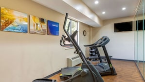 Un gimnasio con cintas de correr, elíptica y bicicleta estática. Hay carteles de motivación en la pared y un reloj.