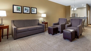 Habitación de hotel con sofá, dos sillones, un pequeño otoman, lámpara y cuadros en la pared.