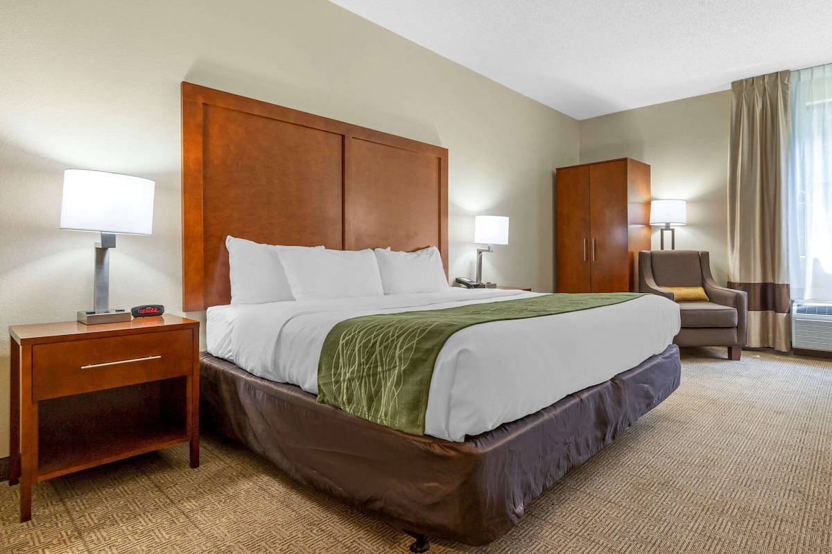 A hotel room with a large bed, a nightstand, a chair, a wardrobe, and two bedside lamps.