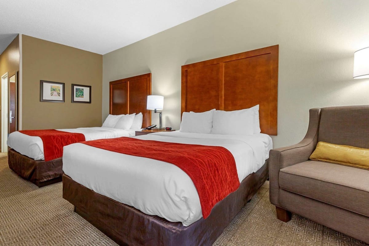 A hotel room with two beds, a sofa, a lamp, and a wall-mounted TV.
