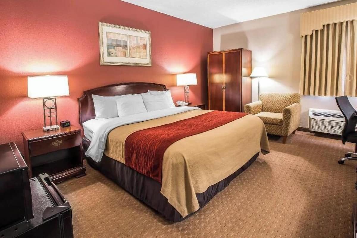 A hotel room with a bed, two bedside lamps, a chair, a desk, and a wardrobe.