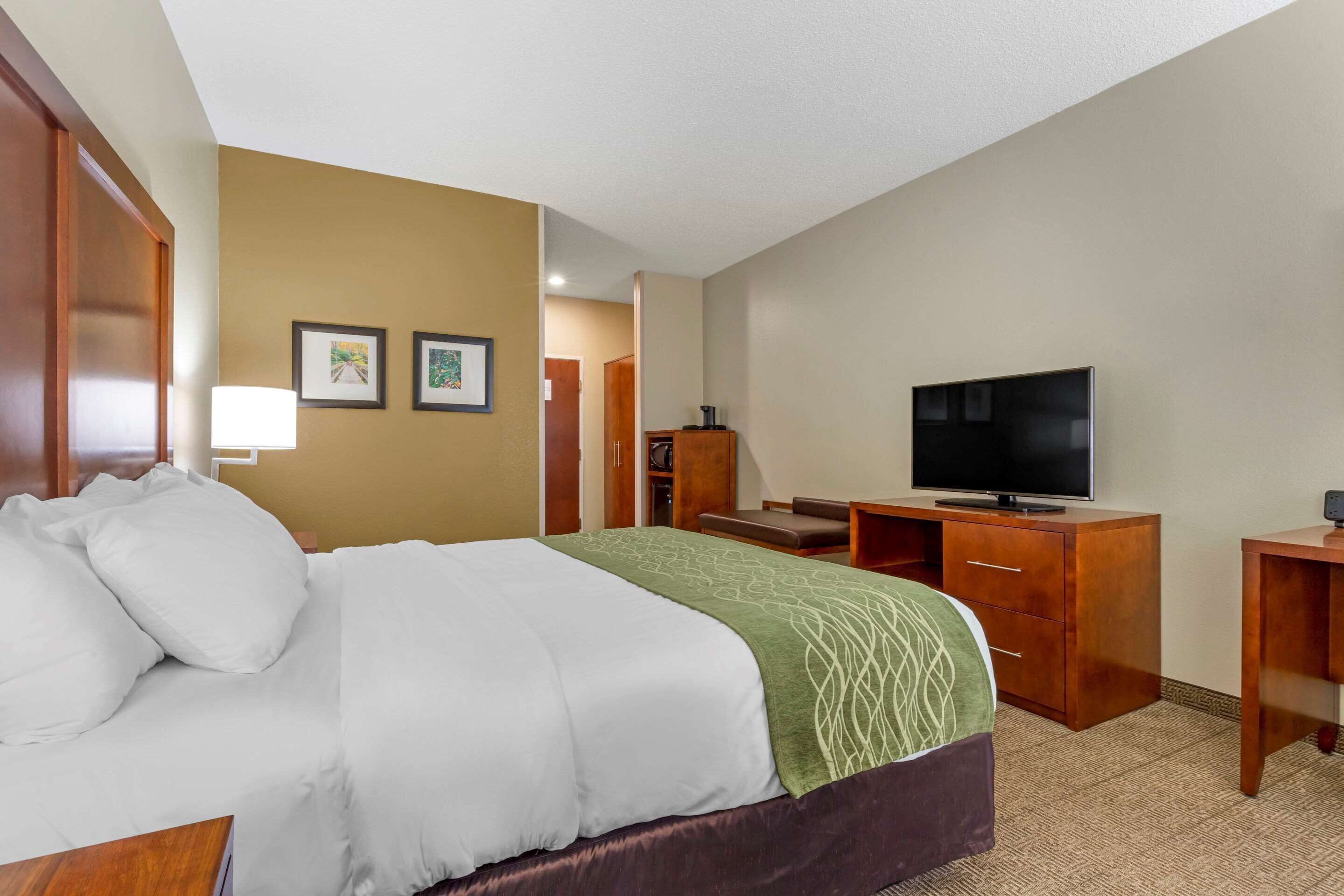 A hotel room with a bed, a desk with a television, and a small seating area.