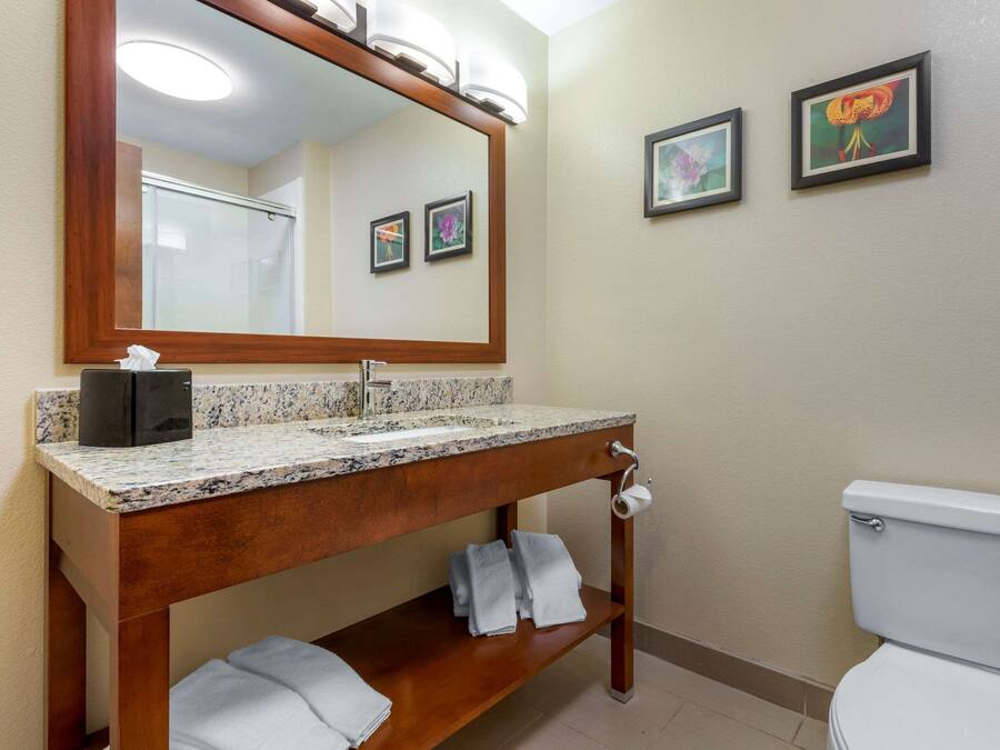 Un baño con tocador de madera, lavamanos, espejo, inodoro y dos cuadros en la pared.