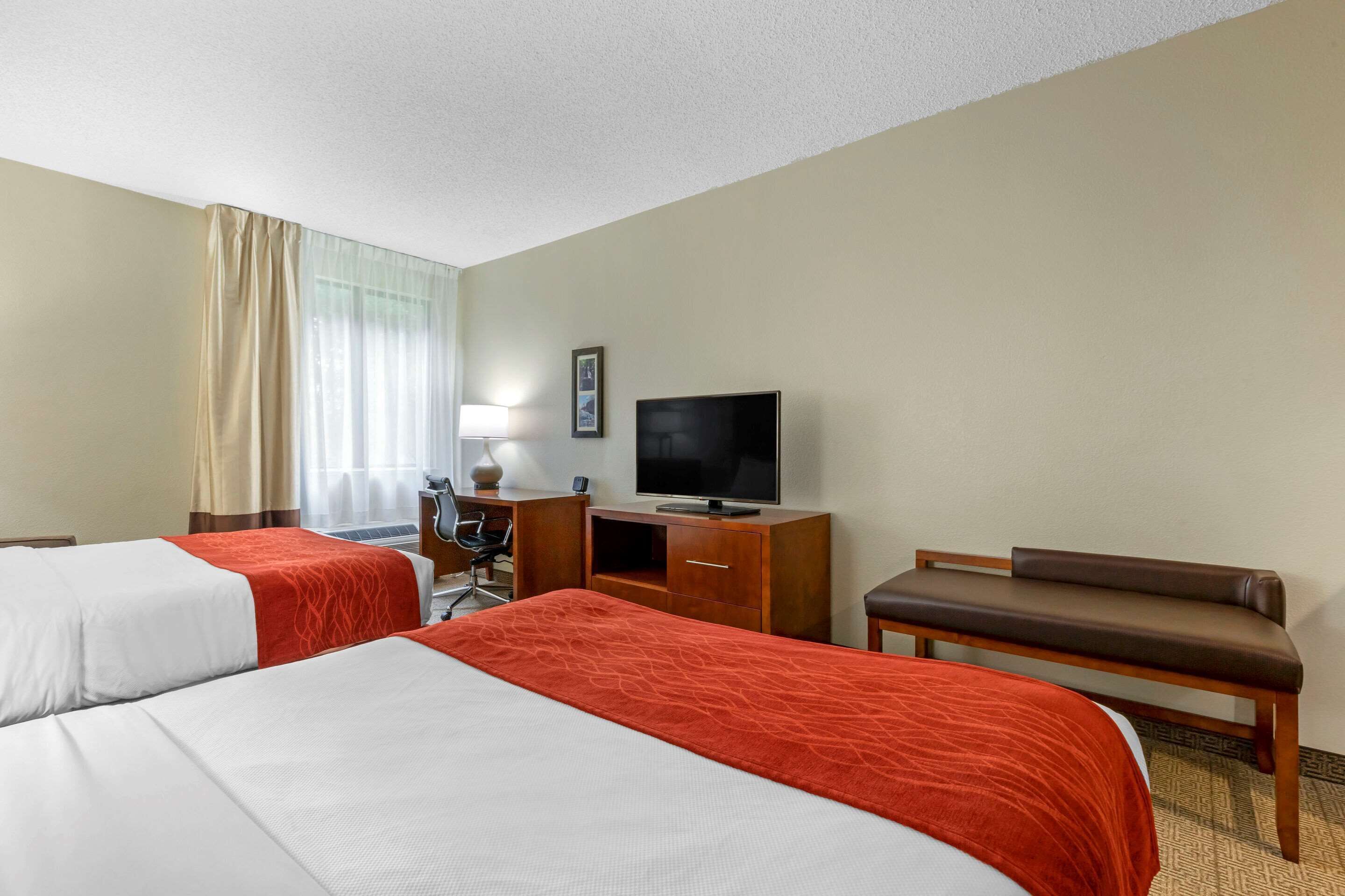 Ett hotellrum med två sängar, ett skrivbord, en tv och en bänk.