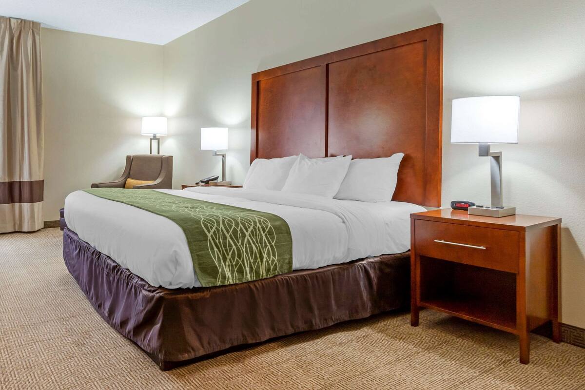 A hotel room with a large bed, two bedside tables, a chair, and a lamp.