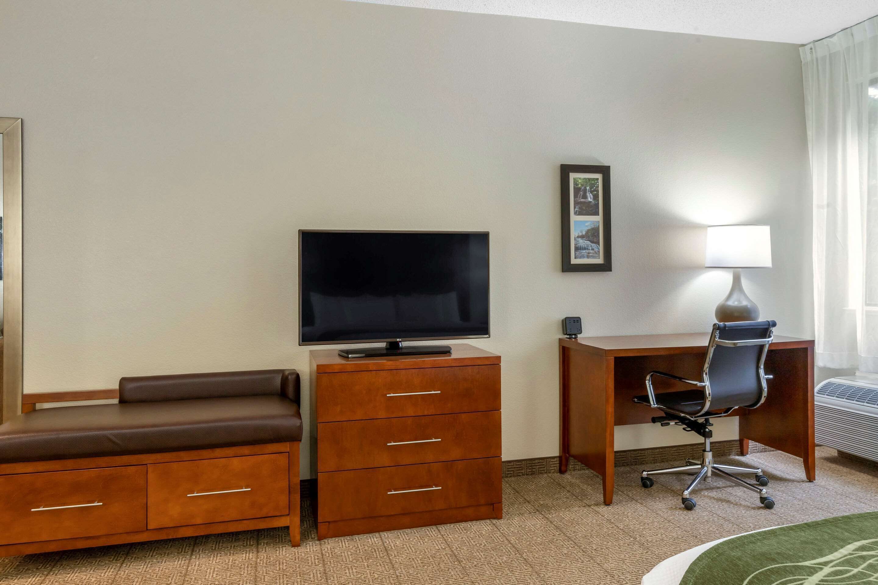 A hotel room with a flat-screen TV, a desk with a chair, a sofa, and a small cabinet.