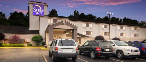 A Sleep Inn hotel with a parking lot, multiple vehicles, and a clear sky.