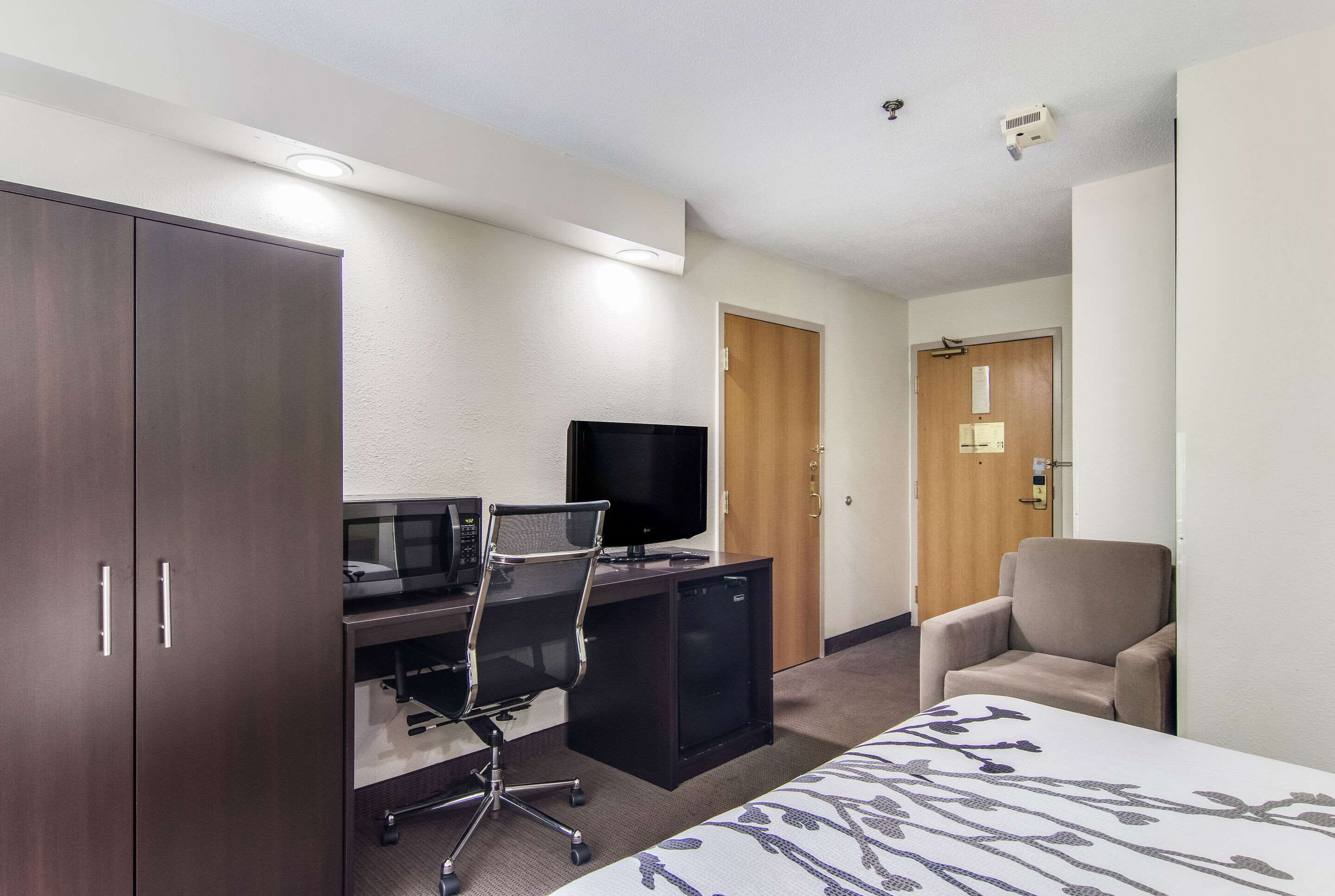 A hotel room with a desk, chair, TV, wardrobe, and a bed.