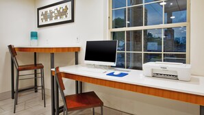 Un espacio de trabajo con un escritorio, dos sillas, una computadora, una impresora y una obra de arte enmarcada en la pared.