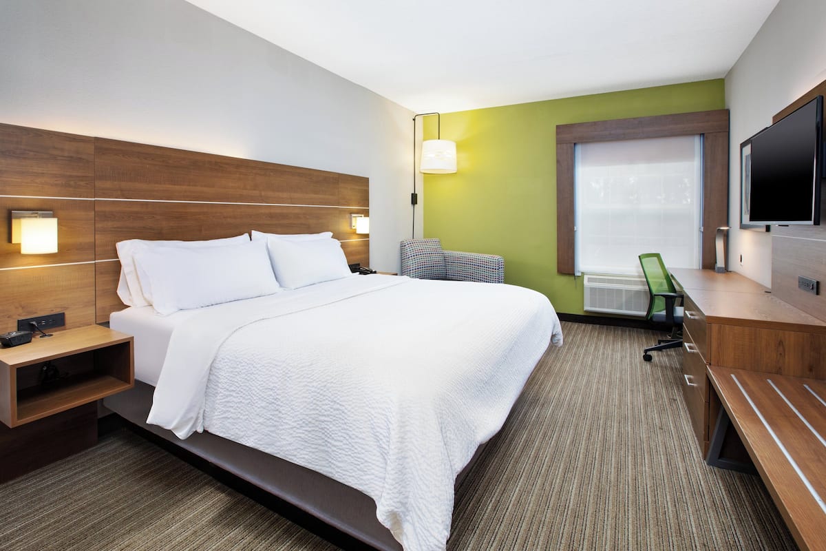 A hotel room with a large bed, bedside tables, a desk with a chair, a television, and a window with blinds.