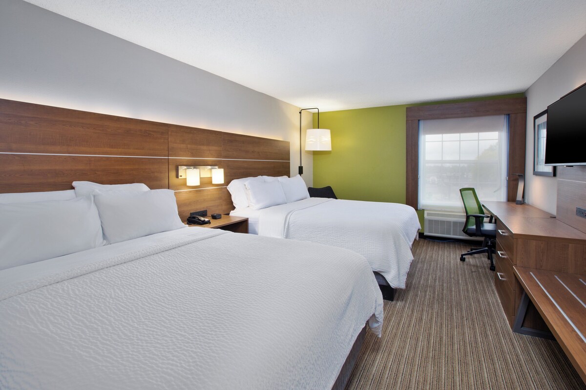 A hotel room with two beds, a desk, a chair, a TV, and a window with a view.