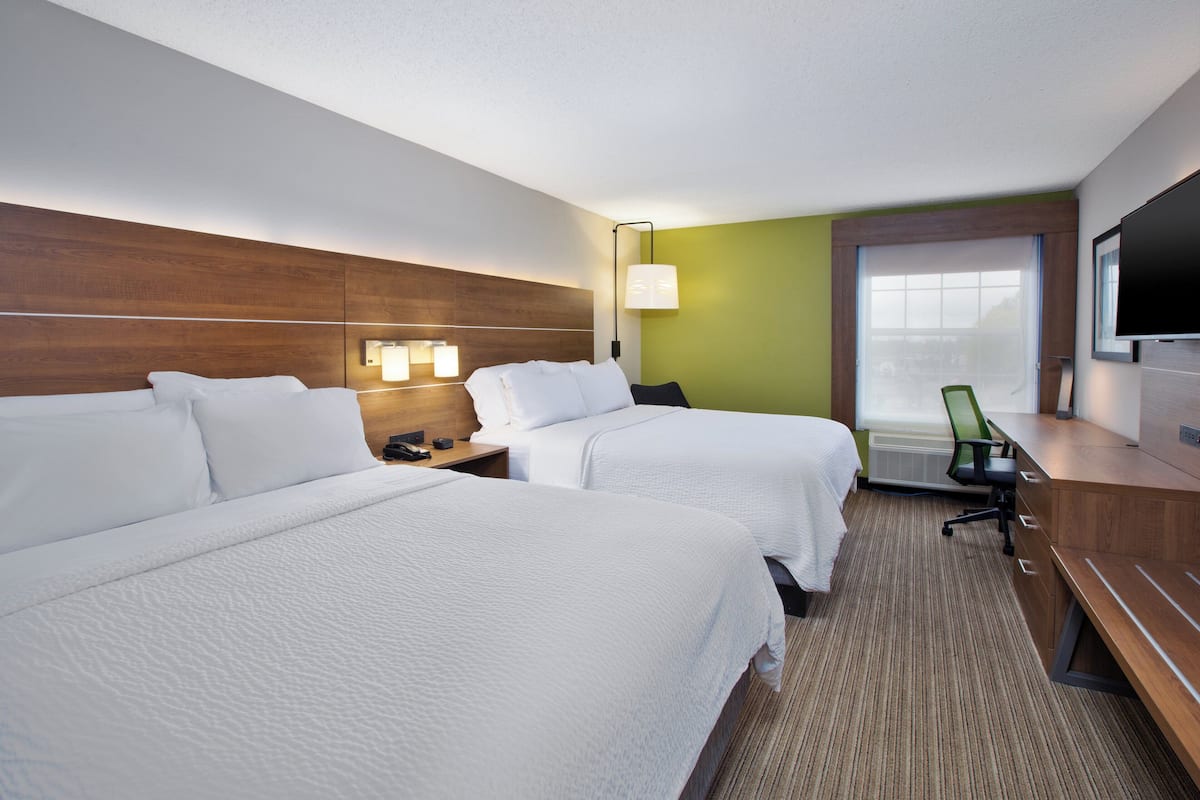 A hotel room with two beds, a desk, a chair, a TV, and a window with a view.