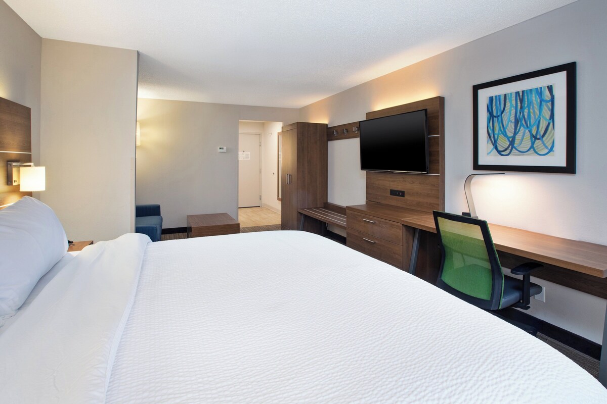 A hotel room with a large bed, a desk with a chair, a flat-screen TV, and a framed abstract painting on the wall.