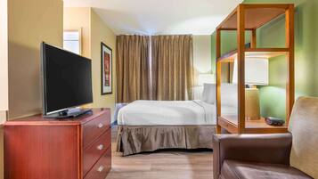 Una habitación de hotel con una cama, un televisor sobre una cómoda de madera, una lámpara y una silla.