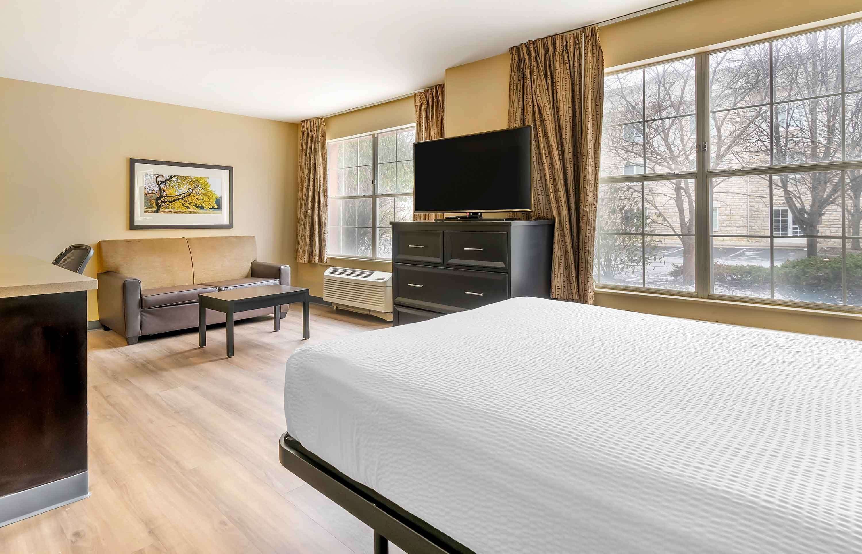 A hotel room with a bed, a TV on a dresser, a sofa, and a desk.