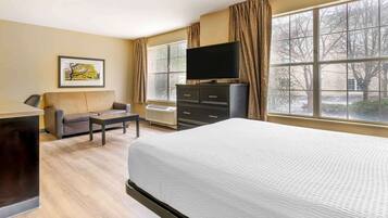 A hotel room with a bed, a TV on a dresser, a sofa, and a desk.
