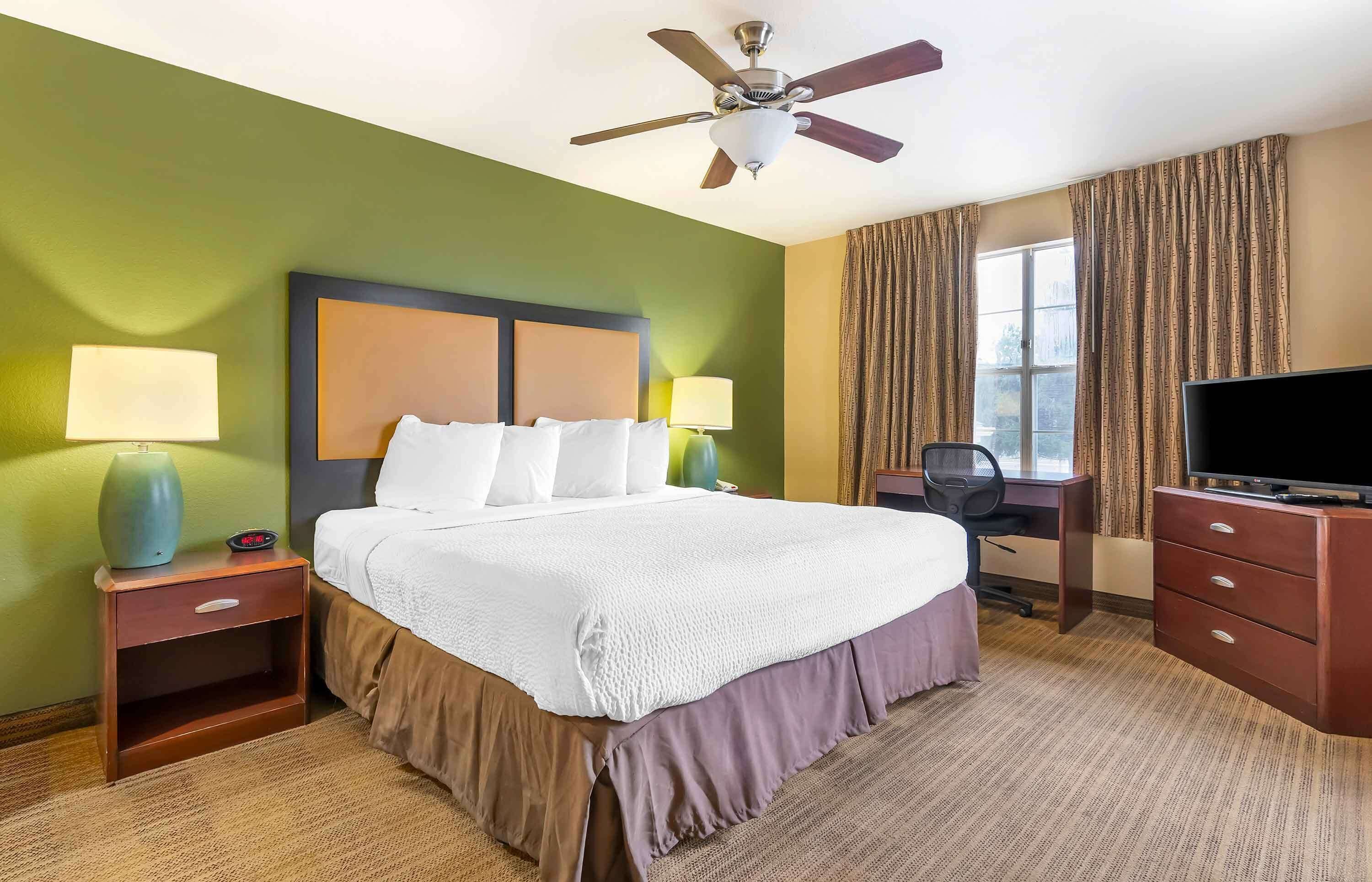 Een hotelkamer met een bed, bureau, televisie en plafondventilator.
