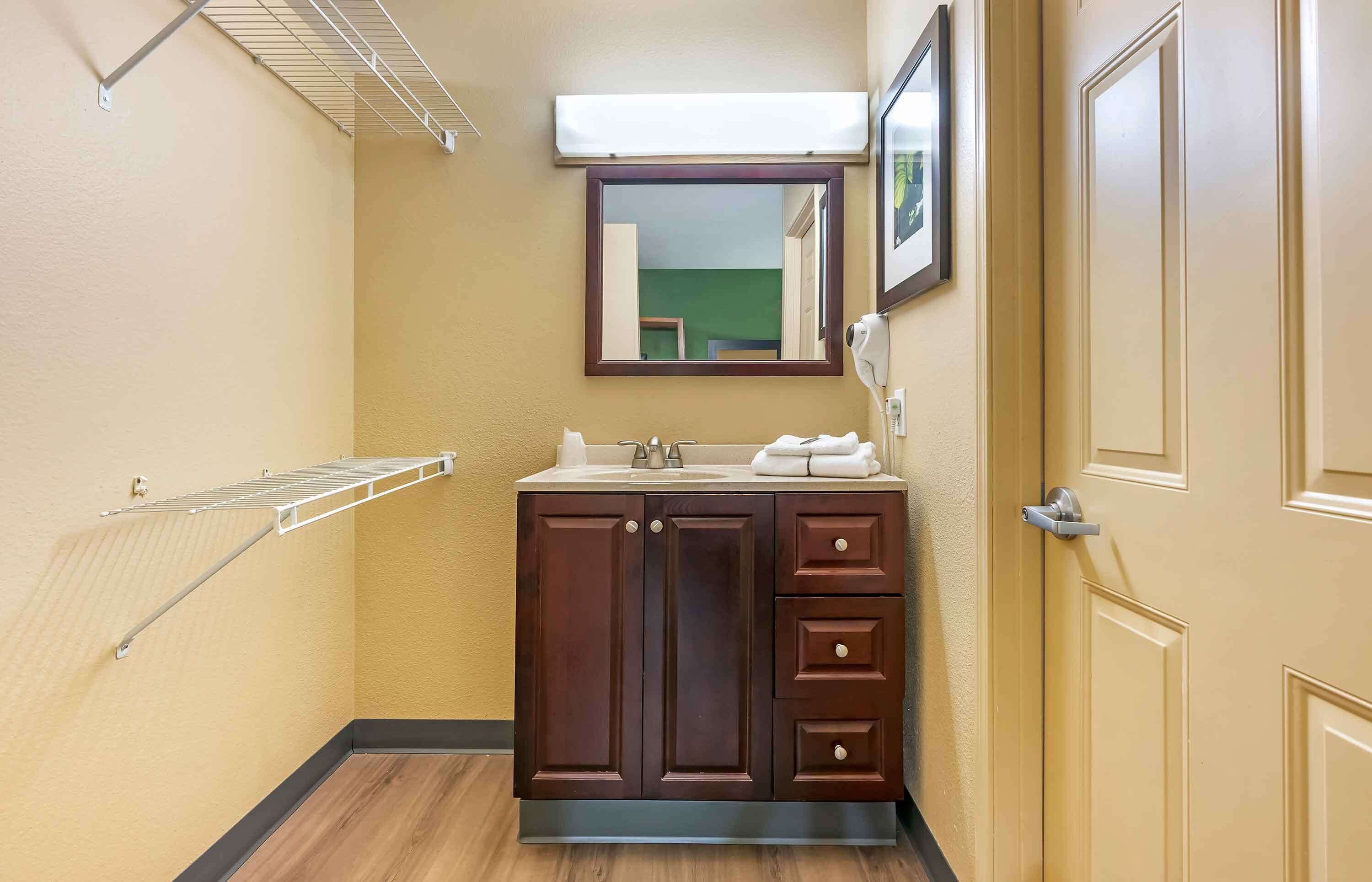 Un baño con tocador de madera, un espejo, toallero y una puerta.