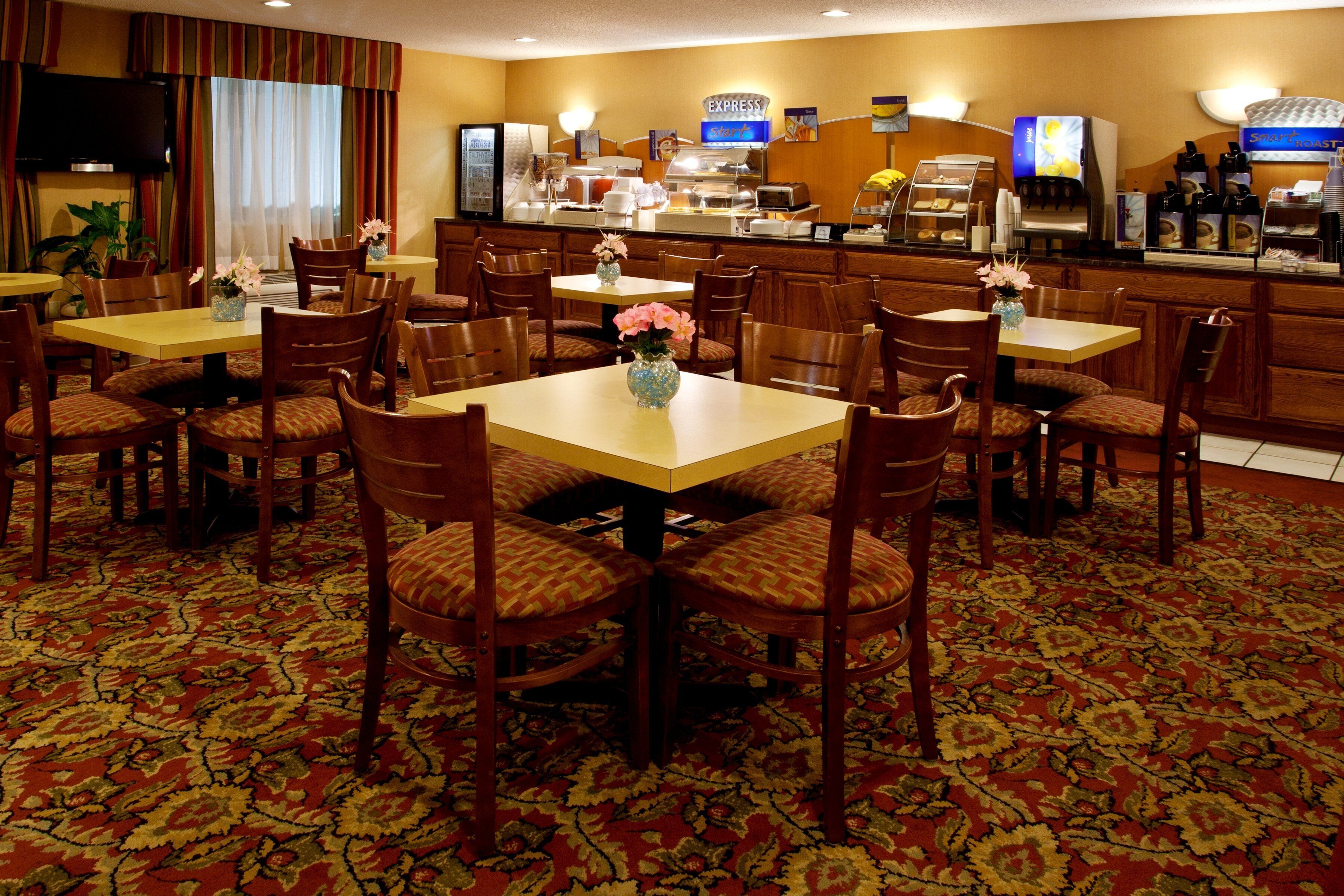 Un comedor de hotel con varias mesas y sillas, una barra de café y una pantalla de televisión.