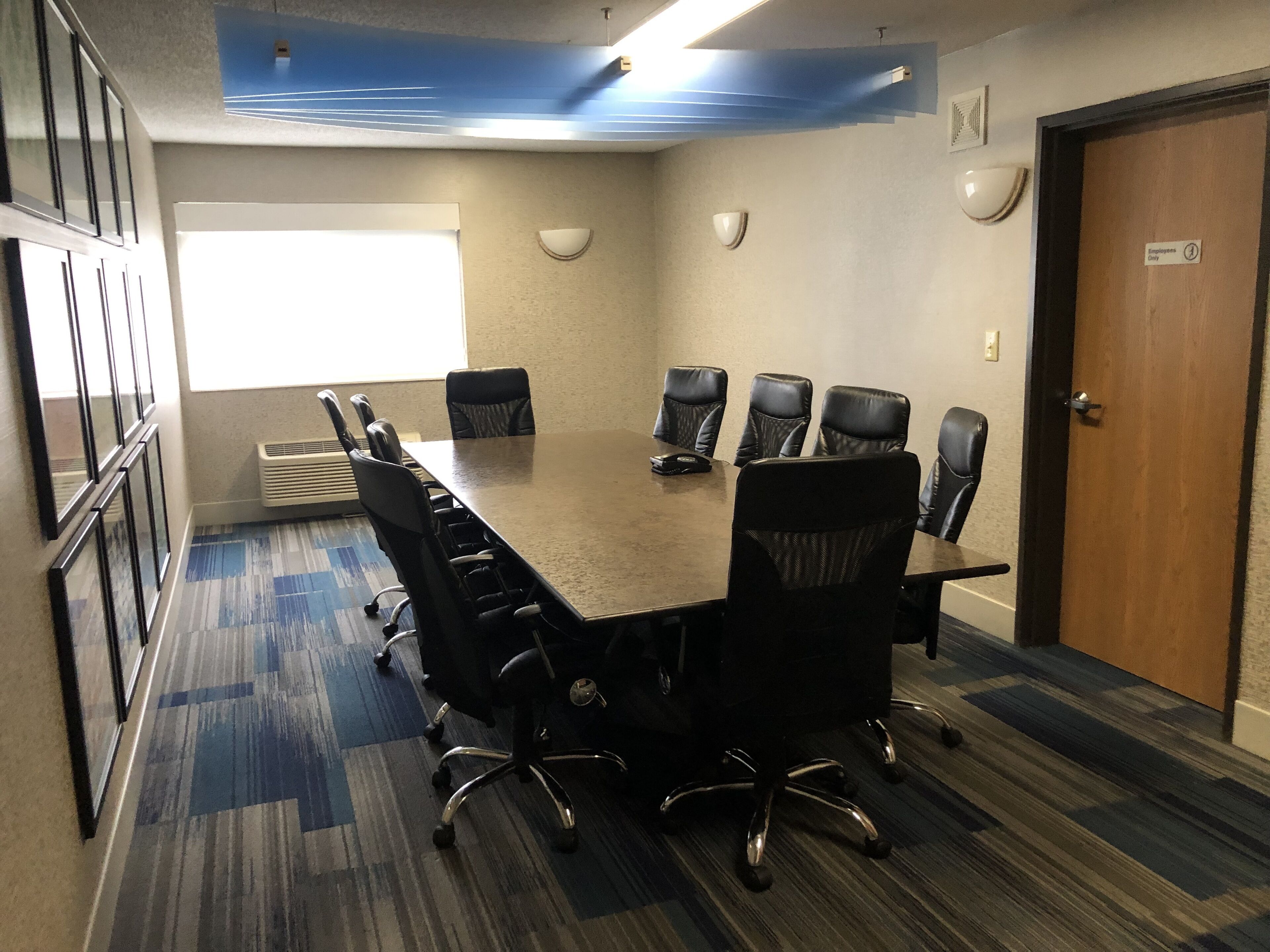 A conference room with a large table, multiple chairs, a door with an 'Employees Only' sign, and a window with blinds.