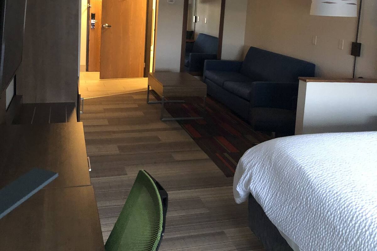 A hotel room with a bed, a sofa, a desk, and a chair. There is a door leading to another room.