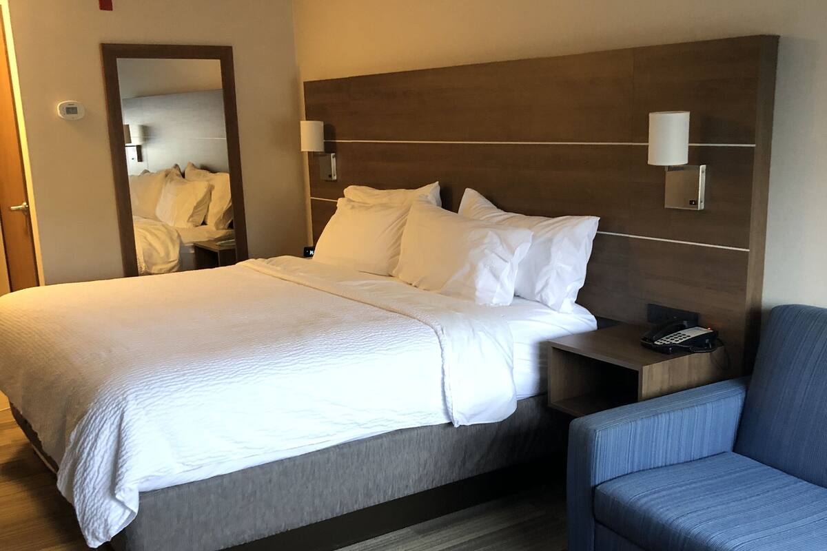 A hotel room with a large bed, a bedside table with a phone, a blue sofa, and a wooden coffee table.