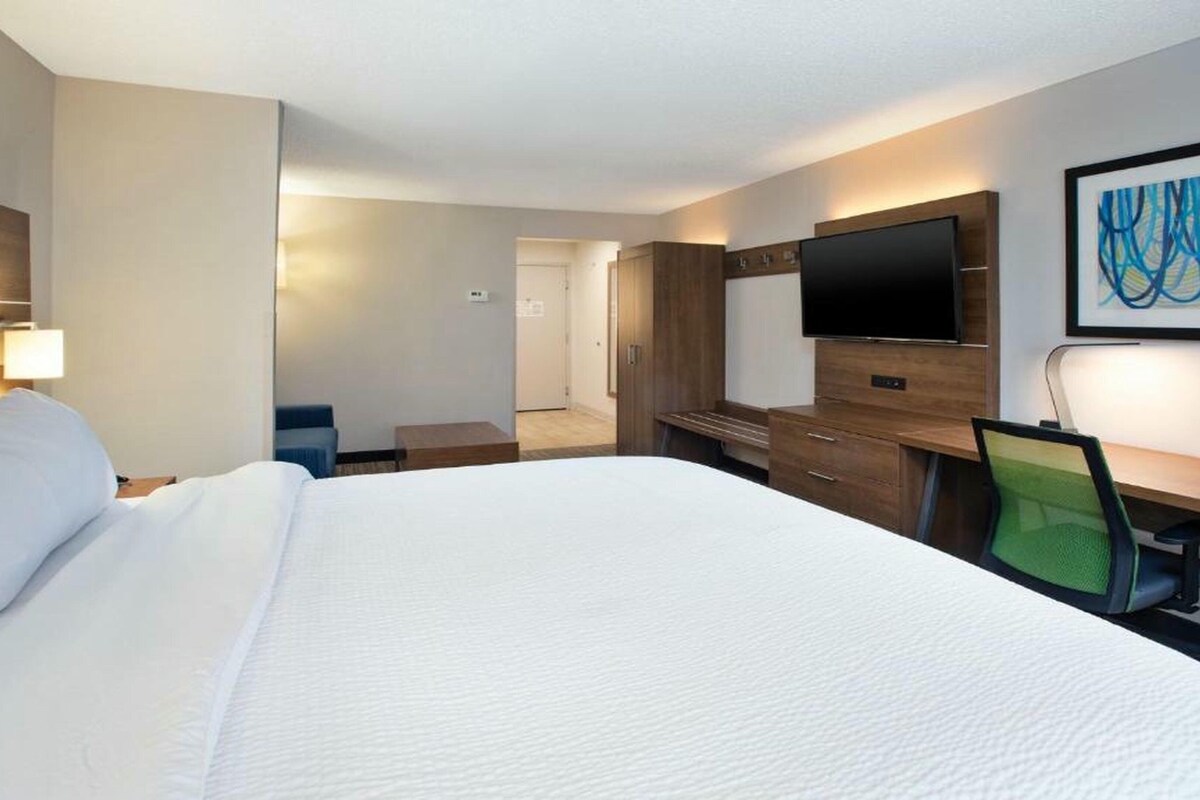 A hotel room with a large bed, a desk, a chair, a TV, and a painting on the wall.