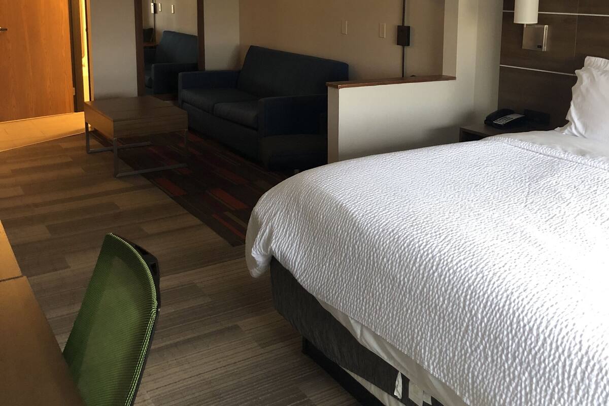 A hotel room with a large bed, a sofa, a desk, and a chair.