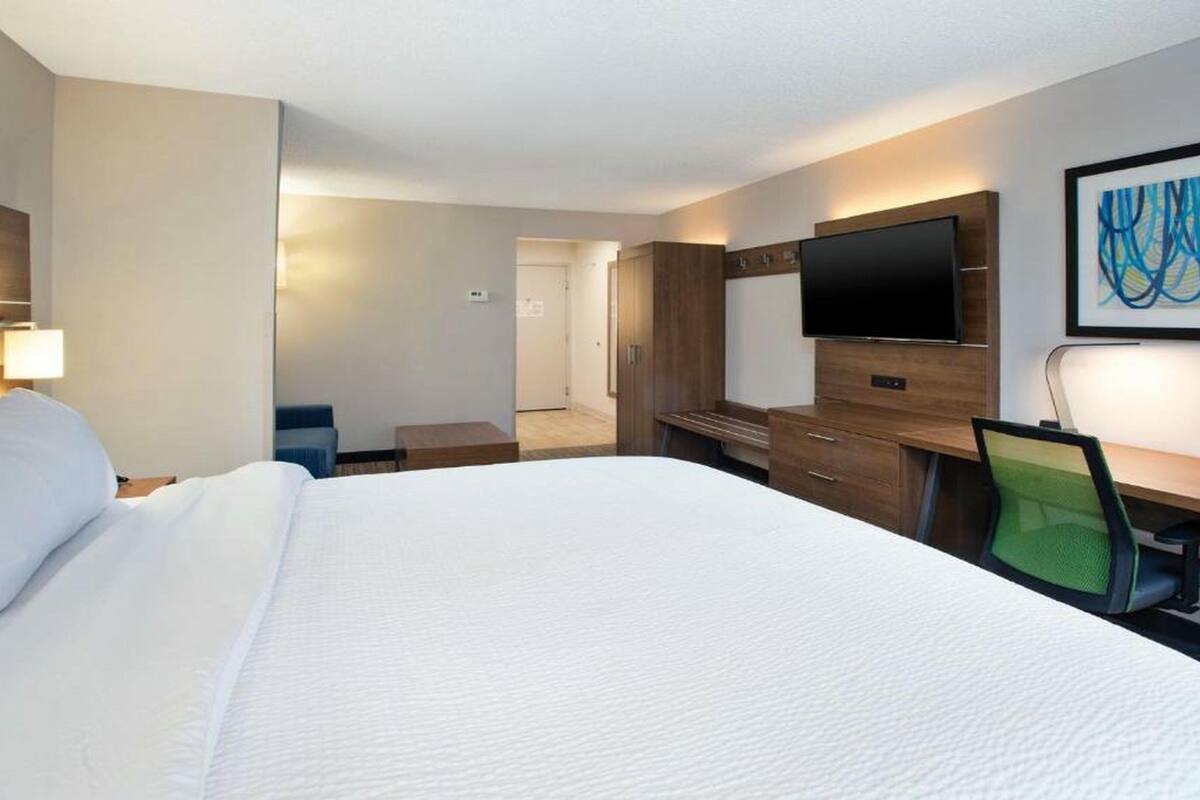 Een hotelkamer met een groot bed, een bureau, een stoel, een televisie en een schilderij aan de muur.