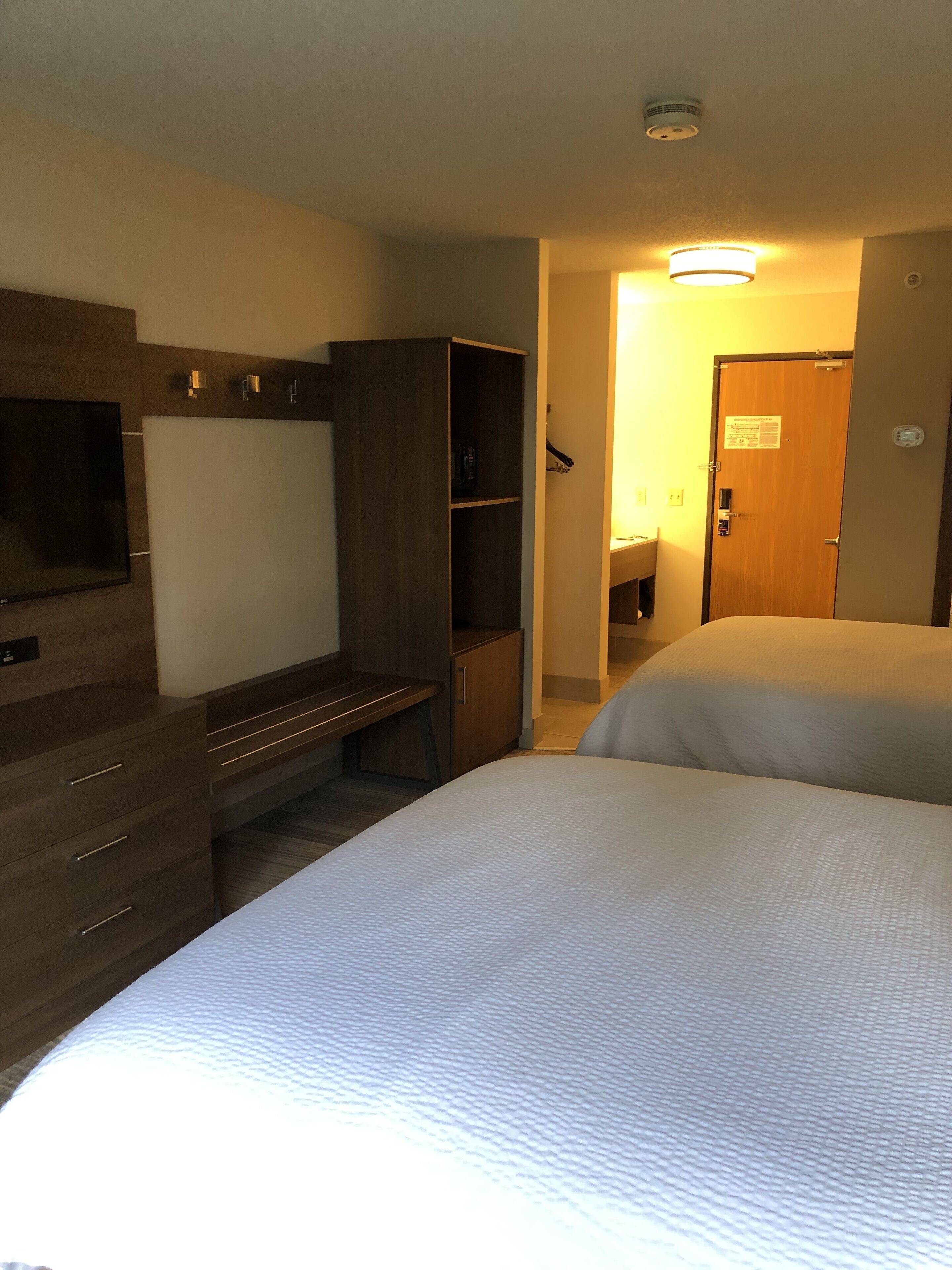 Quarto de hotel com cama, escrivaninha, guarda-roupa, televisão e porta com um aviso.