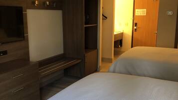 Quarto de hotel com cama, escrivaninha, guarda-roupa, televisão e porta com um aviso.
