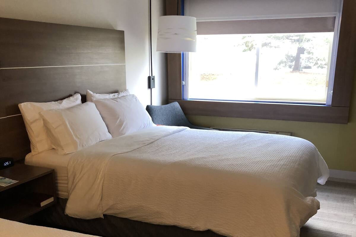A hotel room with two beds, a nightstand, a lamp, and a window with a view of the outdoors.