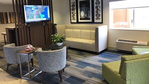 A modern hotel lobby with a sofa, chairs, a small table with a plant, a TV displaying a weather forecast, and framed artwork on the wall. - Holiday Inn Express Mt Vernon by IHG (Mount Vernon)