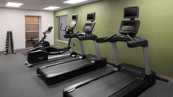 Une salle de sport équipée de tapis de course, de vélos d’exercice et d’un banc de musculation.