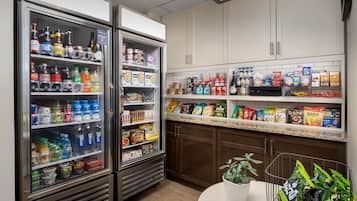 Una cocina con dos refrigeradores llenos de bebidas, una encimera con aperitivos envasados y una planta en una mesa redonda.