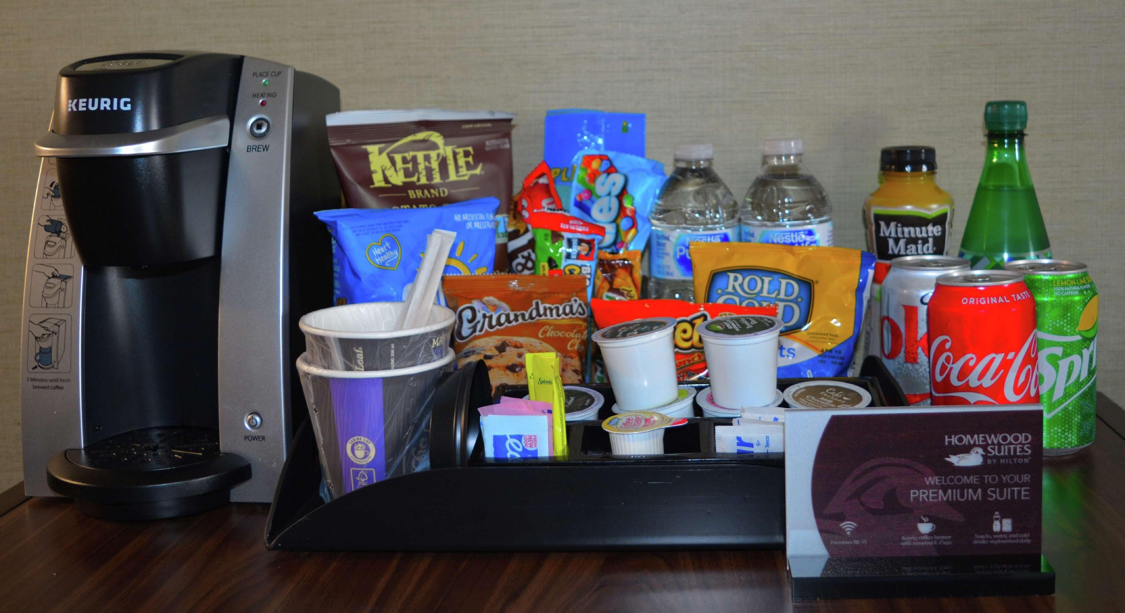 A coffee maker, assorted snacks, bottled water, and soda cans on a tray.