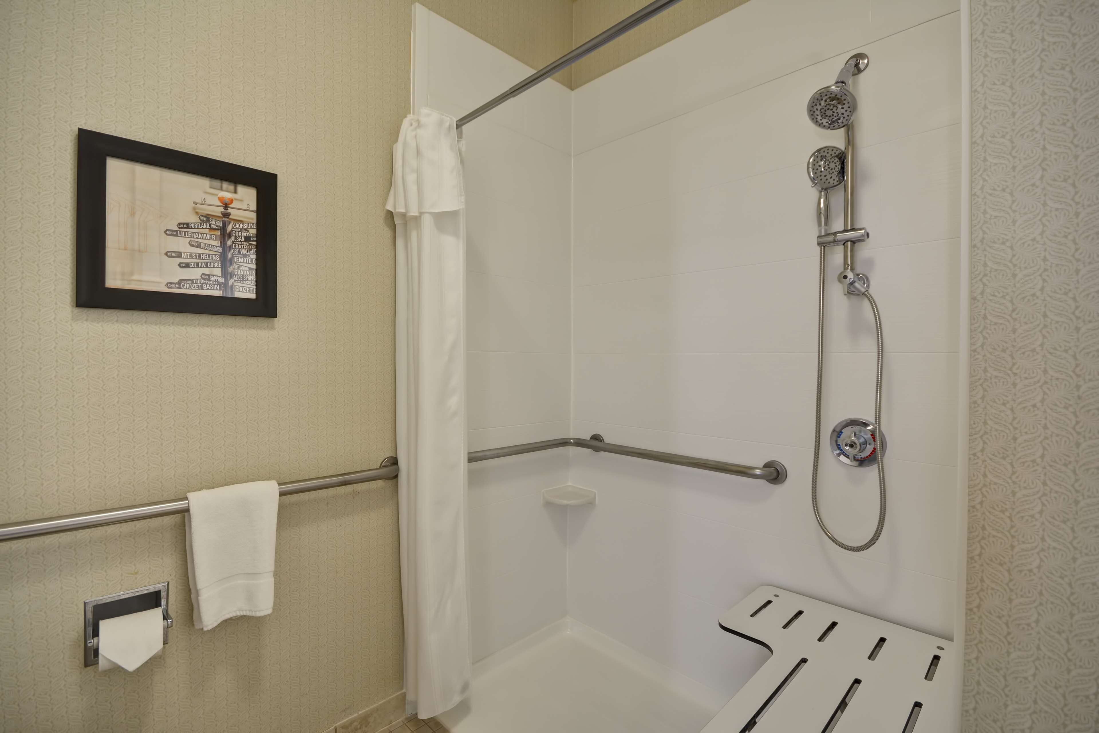 A shower area with a handheld showerhead, a towel rack, and a framed sign on the wall.